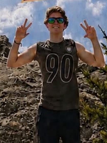 Duncan smiling outdoors in a number 90 jersey and sunglasses, making peace signs against a blue sky